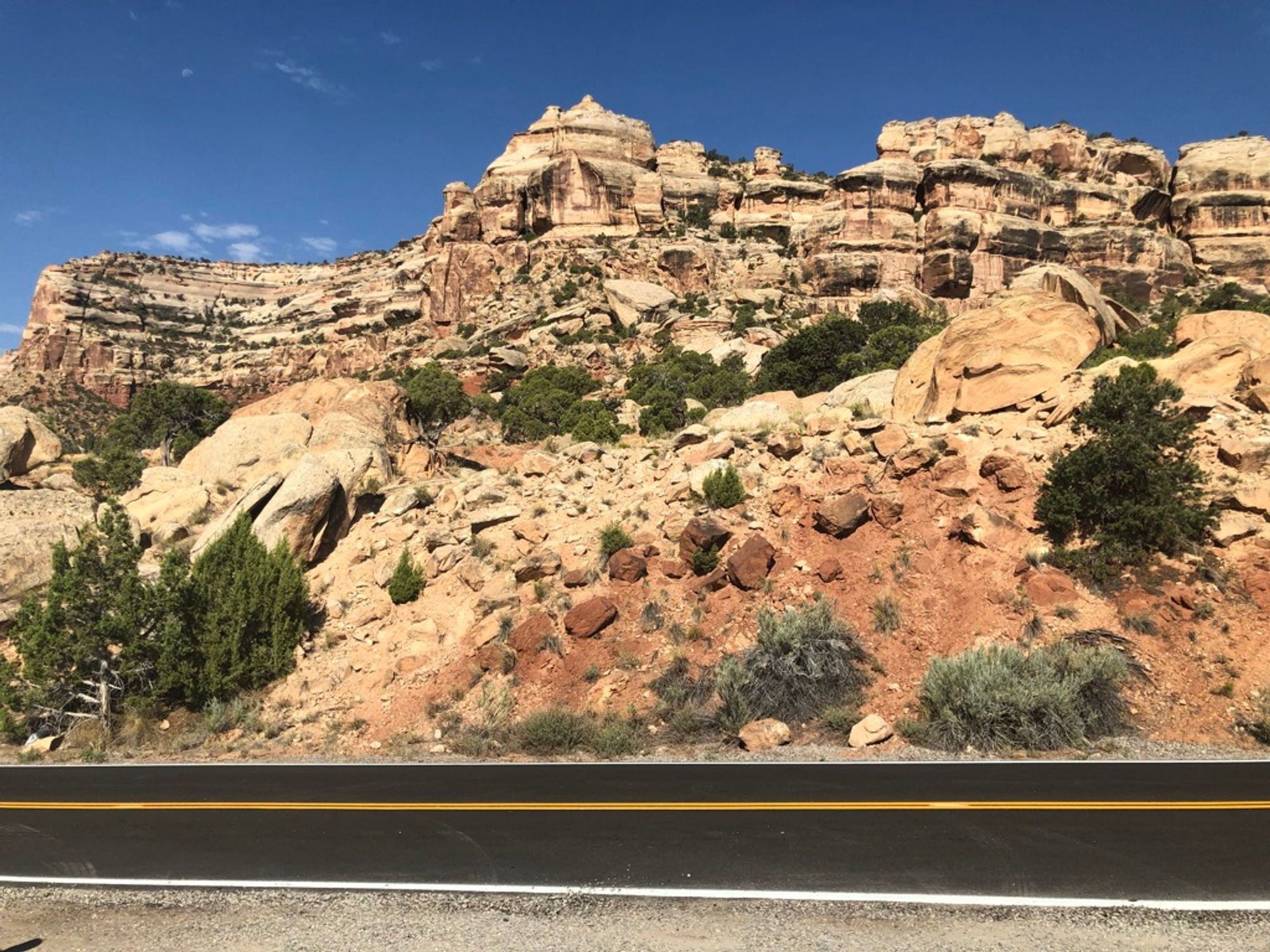 Fresh asphalt in the foreground and tan rock formations taking up most of the background